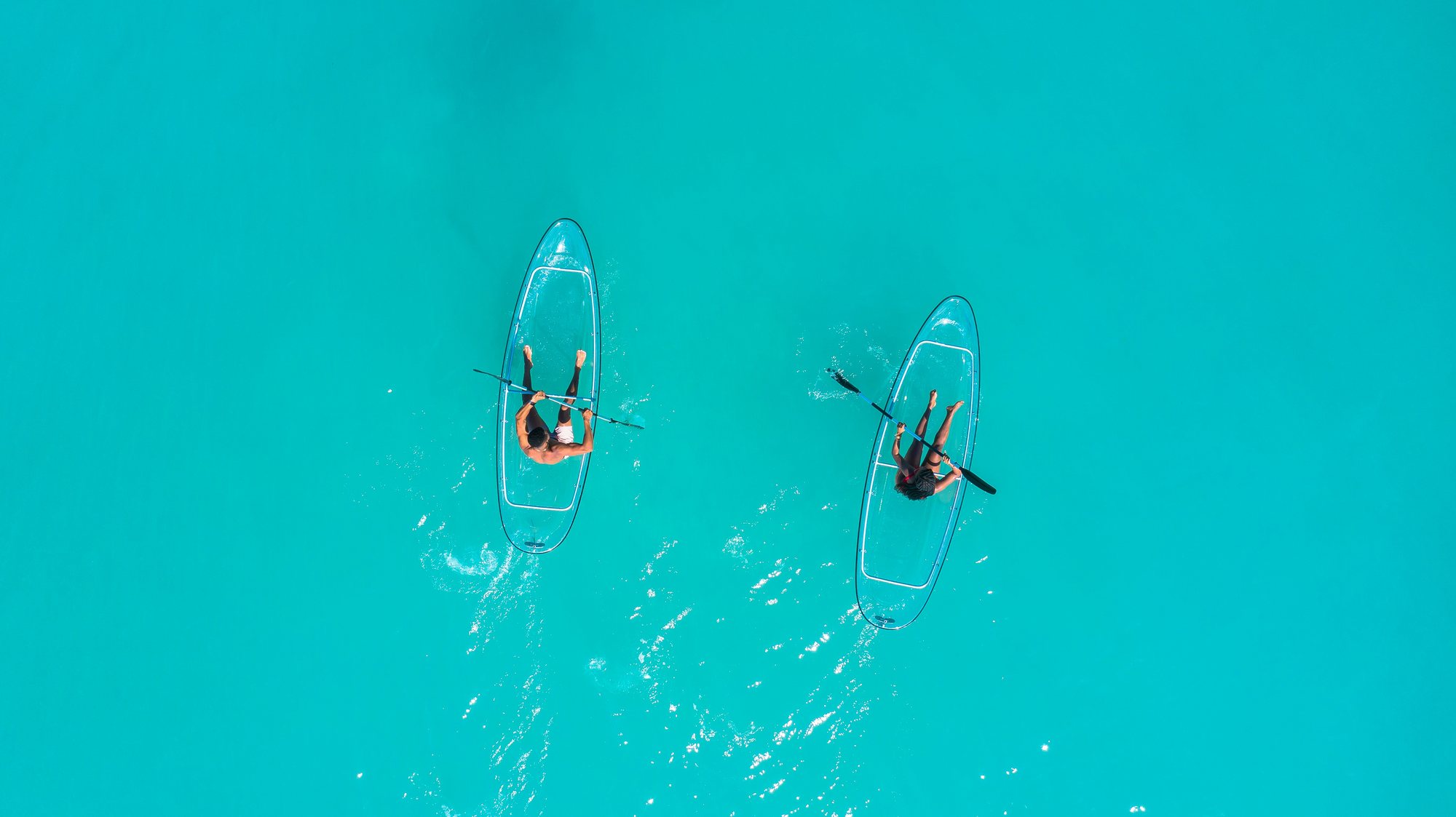 Two people paddling clear kayaks over turquoise water in Grenada
