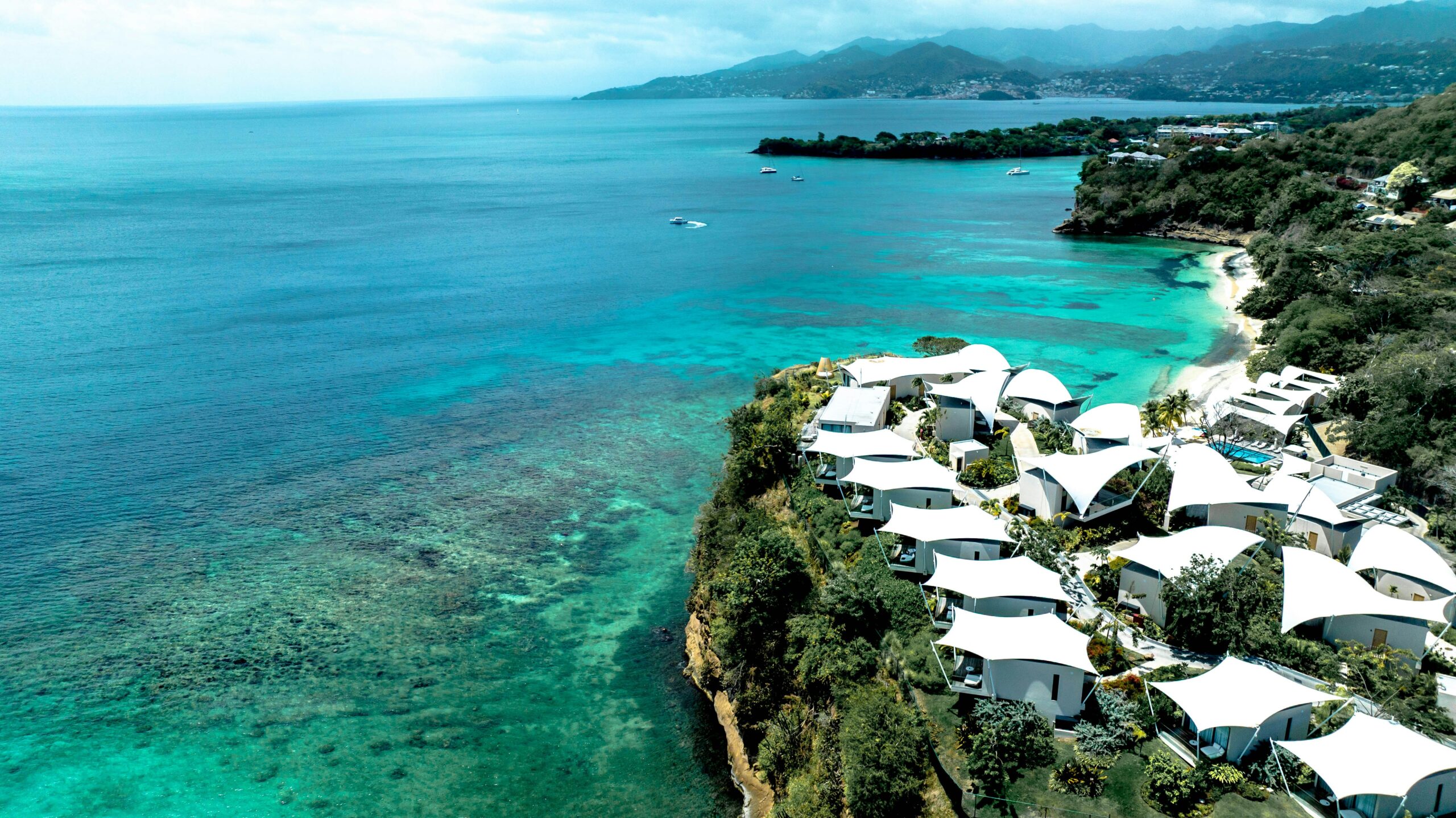 Aerial view of white cottages on a green hillside above a reef-fringed bay in Grenada